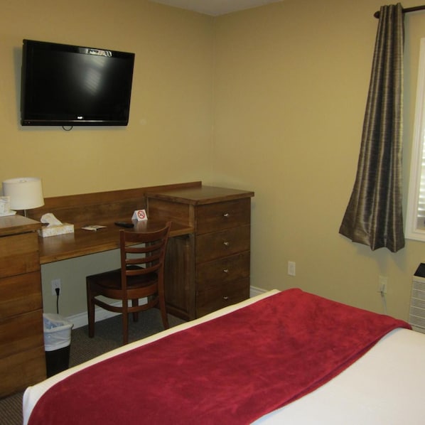 A hotel room with a bed, a desk, a chair, a television, and a window with curtains. - Reynolds Hotel (Lillooet)