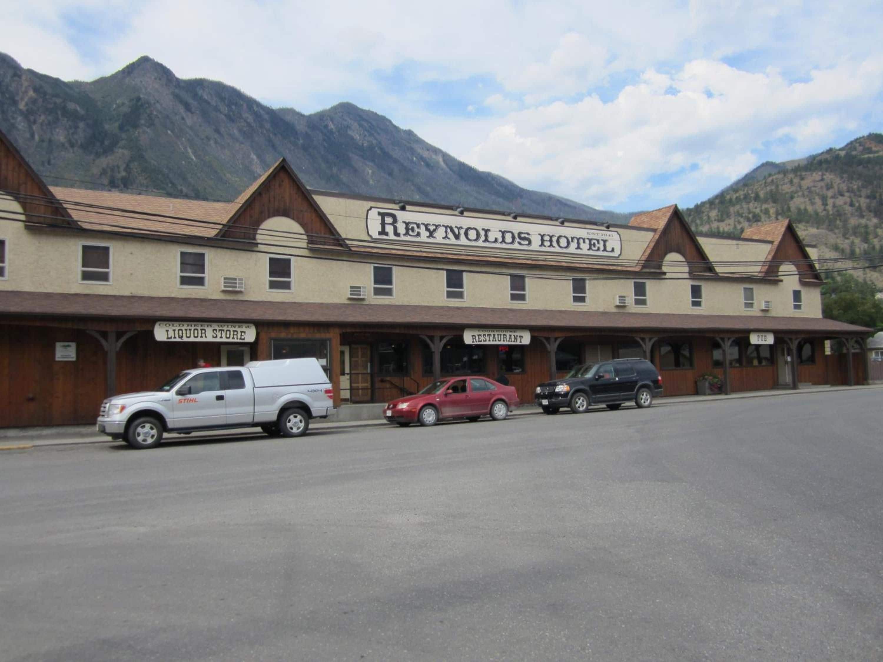 A two-story building with a sign for the Reynolds Hotel. There are parked vehicles in front.