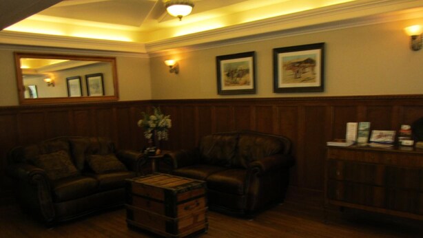 A room with two leather sofas, a wooden coffee table, a mirror, framed pictures on the wall, and a wooden cabinet with items on top. - Reynolds Hotel (Lillooet)