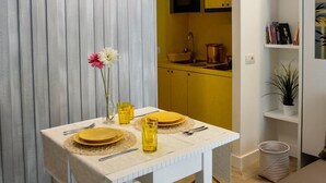 A dining area with a table set for two, a kitchen in the background, and a bookshelf with books and decorative items. - Click&Sleep (Naples)