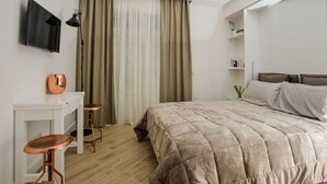 A modern bedroom with a large bed, a desk with two stools, a TV mounted on the wall, and a window with curtains. - Click&Sleep (Naples)