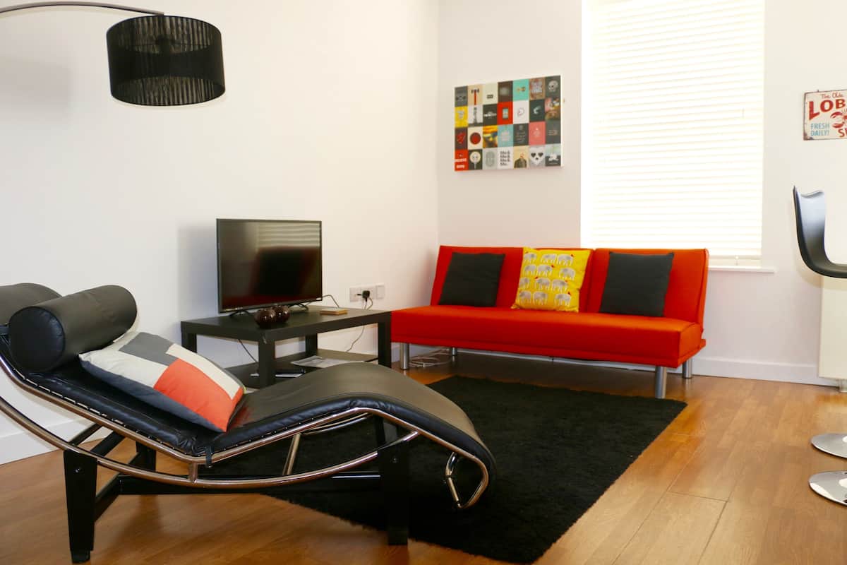 A modern living room with a reclining chair, a red sofa, a flat-screen TV, and a wall art piece.