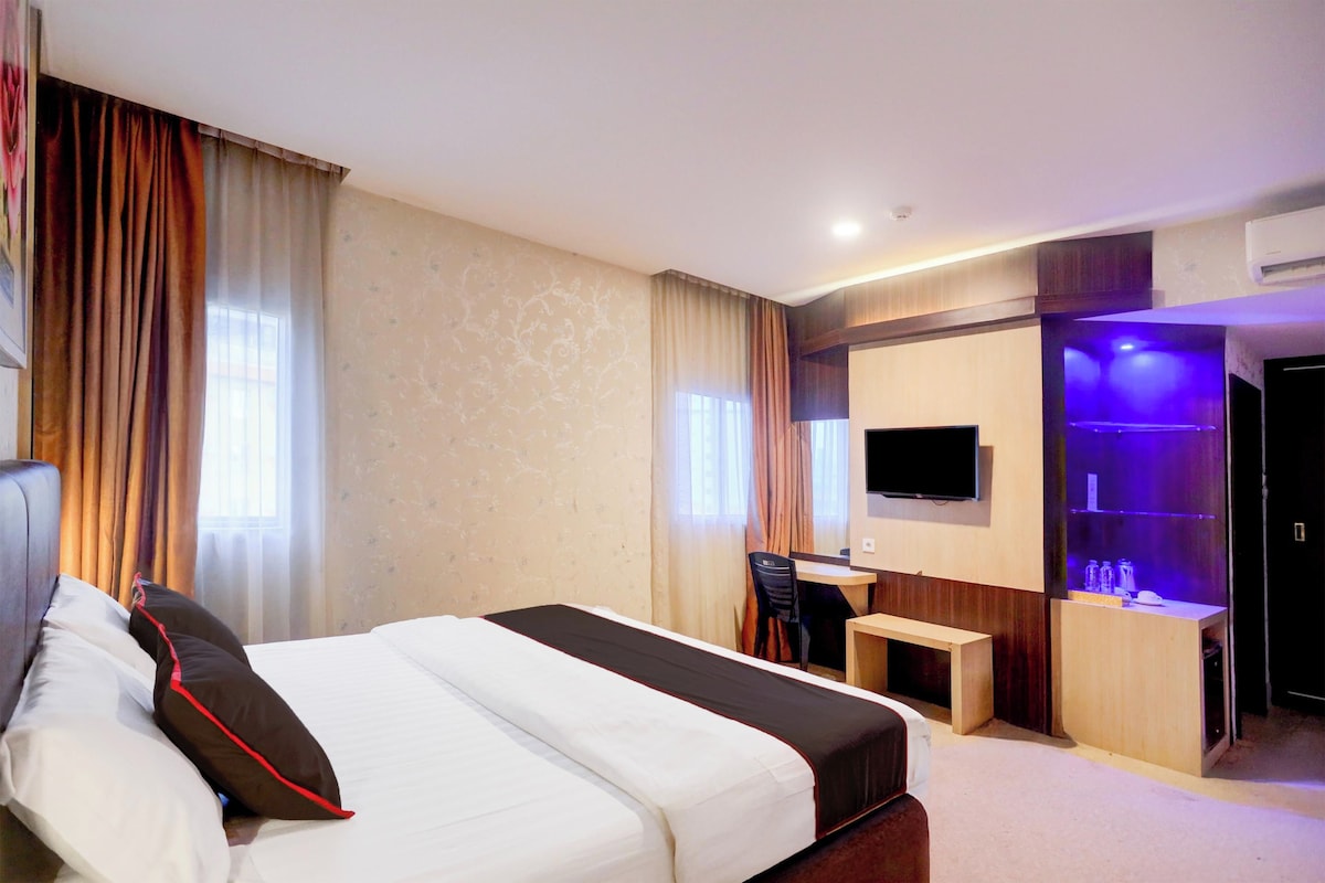 A hotel room with a bed, a desk, a chair, a television, and a minibar.
