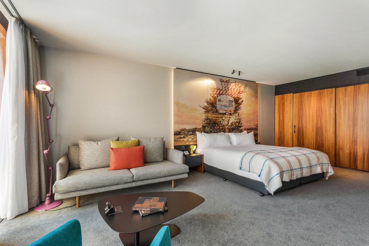 Quarto de hotel moderno com cama, sofá, mesa de centro e um quadro na parede.