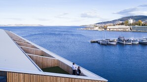 A modern building with a wooden exterior and a balcony overlooking a marina with boats. - MACq 01 Hotel (Hobart)