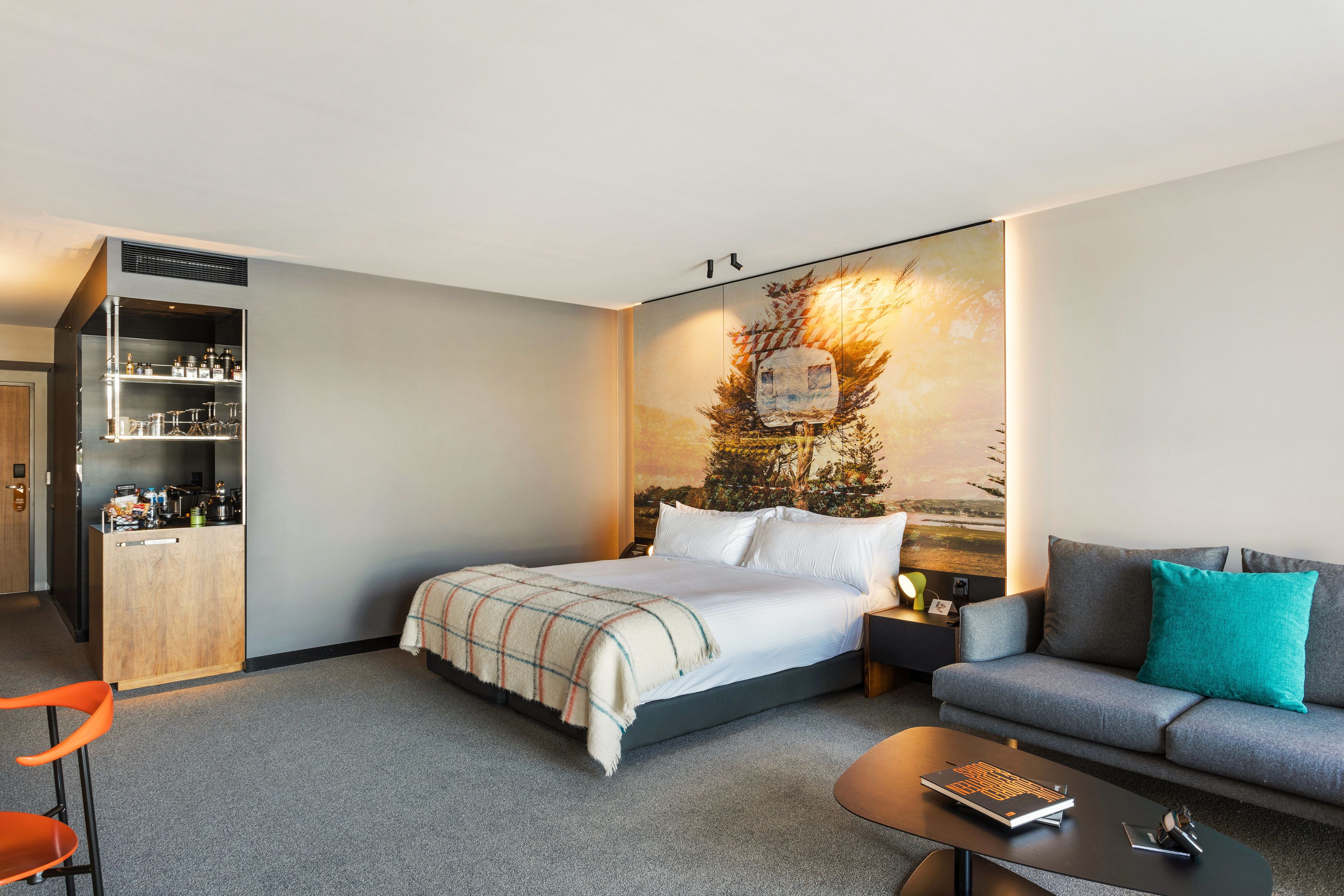 A hotel room with a bed, a sofa, a coffee table, a desk, and a bookshelf.