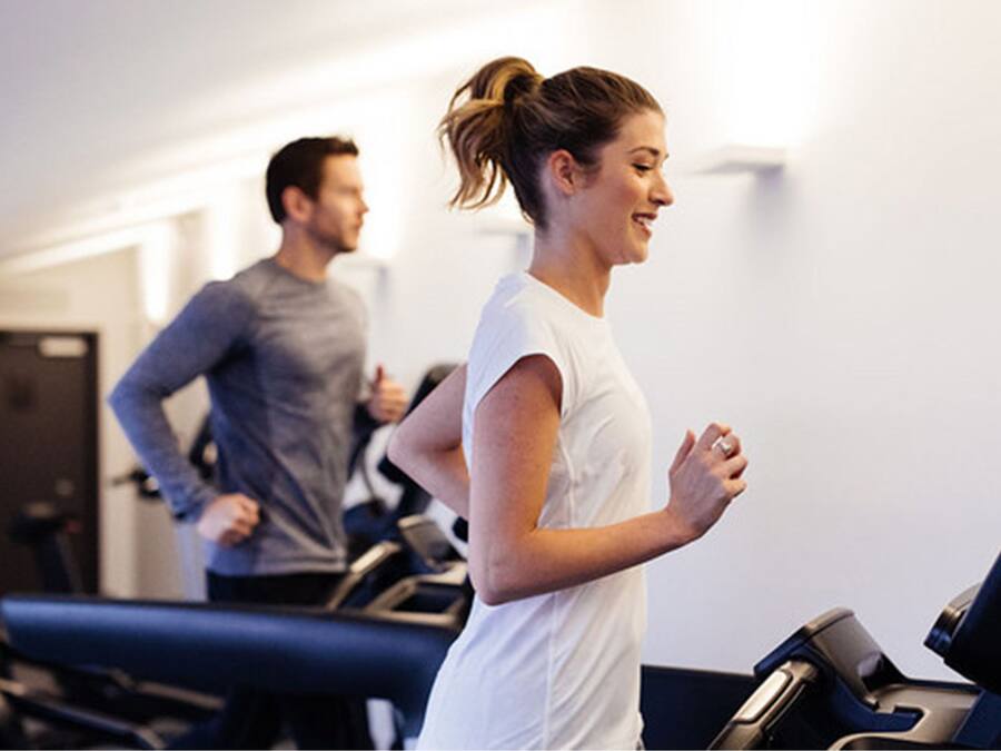 Un gimnasio con cintas de correr y una persona corriendo.