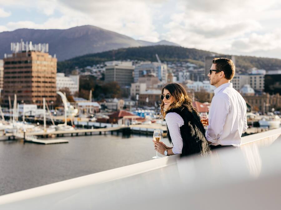 A couple overlooking a marina with boats and buildings in the background.