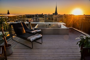 A rooftop terrace with a lounge chair, a small table, and a hot tub.