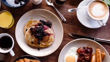 En frukostuppläggning med pannkakor, ägg, bacon, korv och en croissant på ett träbord.