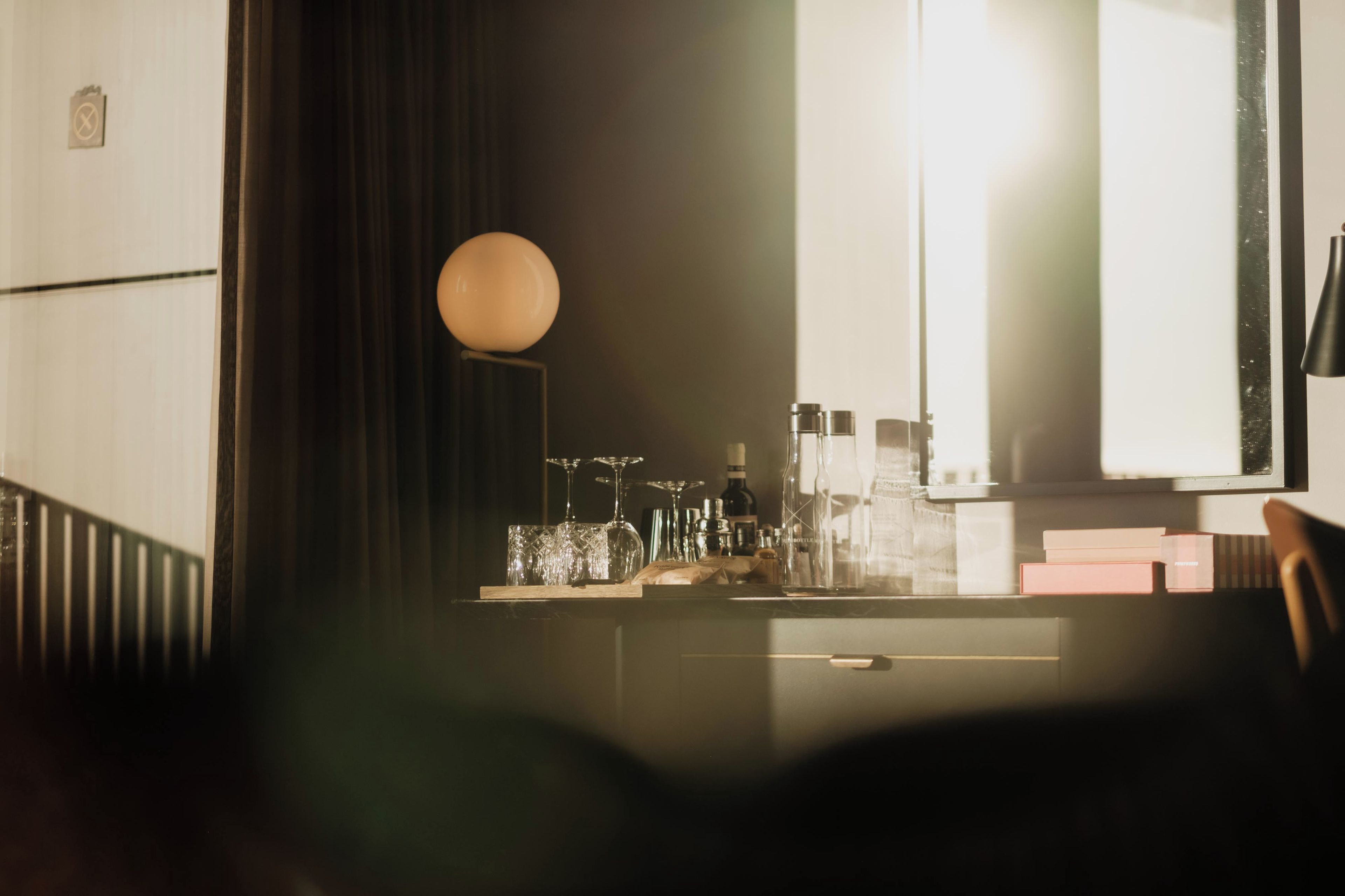 Una habitación tenuemente iluminada con un escritorio, una lámpara y varios botellas y vasos.