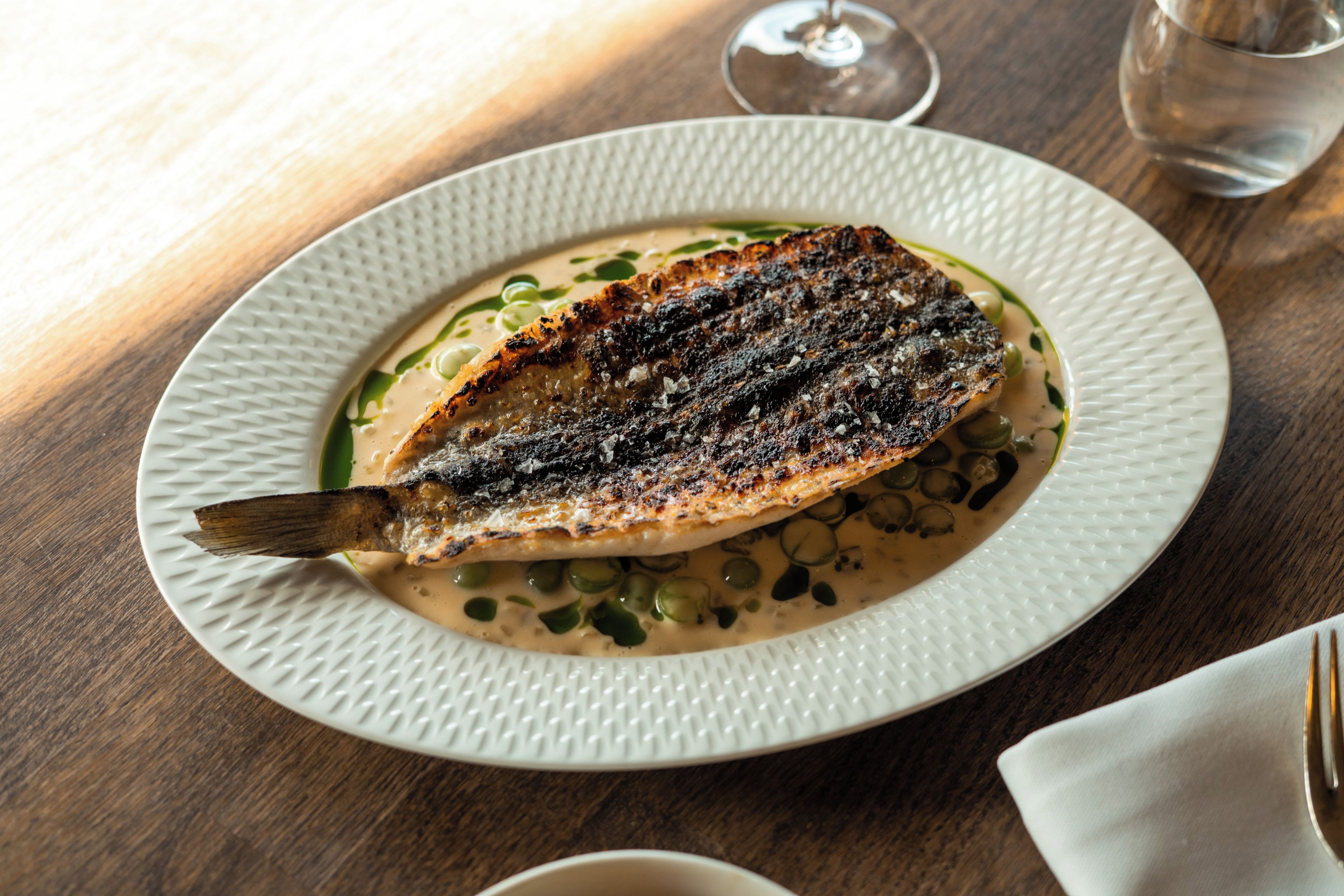 Une assiette blanche sur laquelle repose un poisson grillé, le tout posé sur une surface texturée.