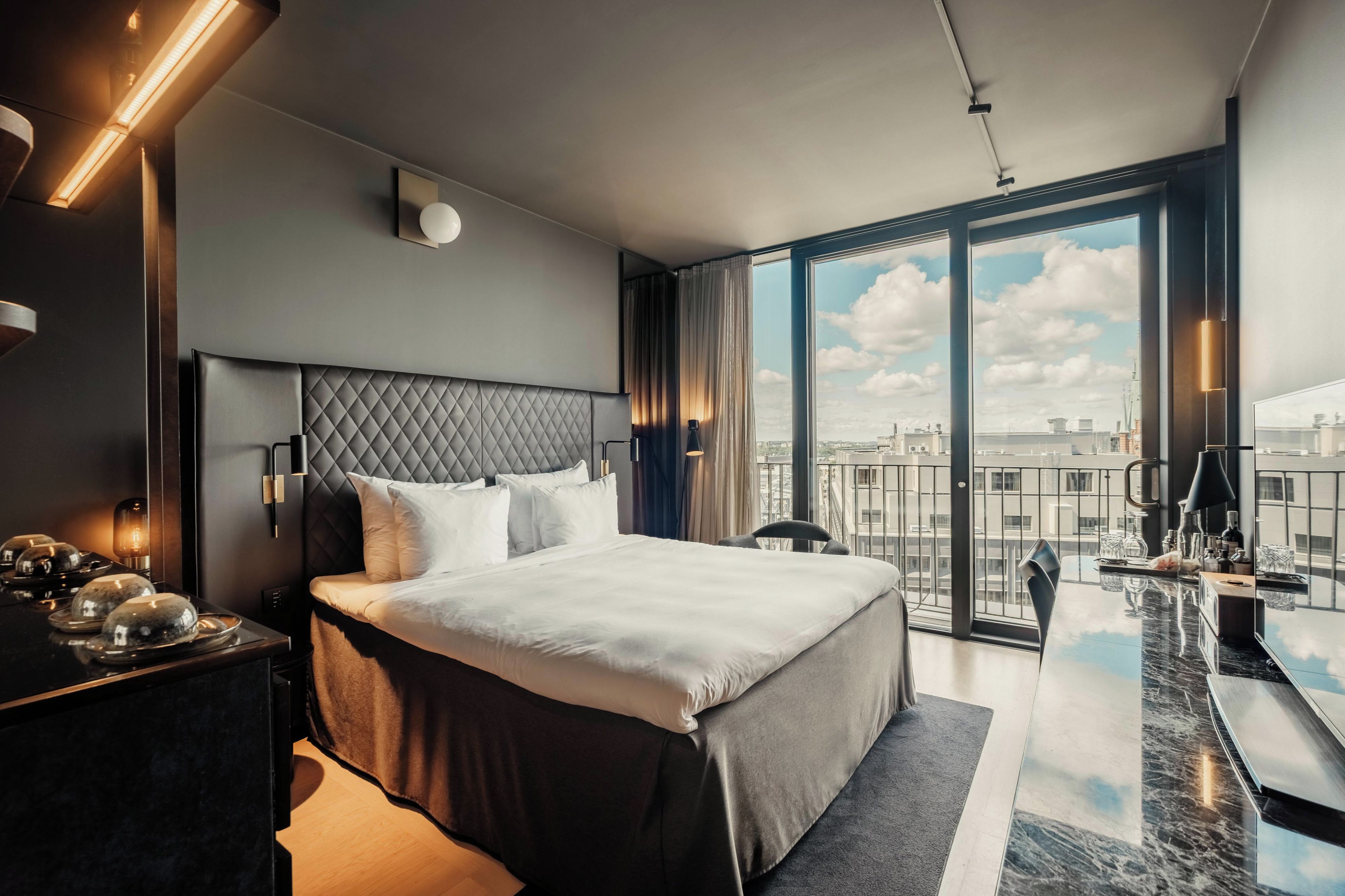 A modern hotel room with a large bed, a desk with a view, and a balcony.