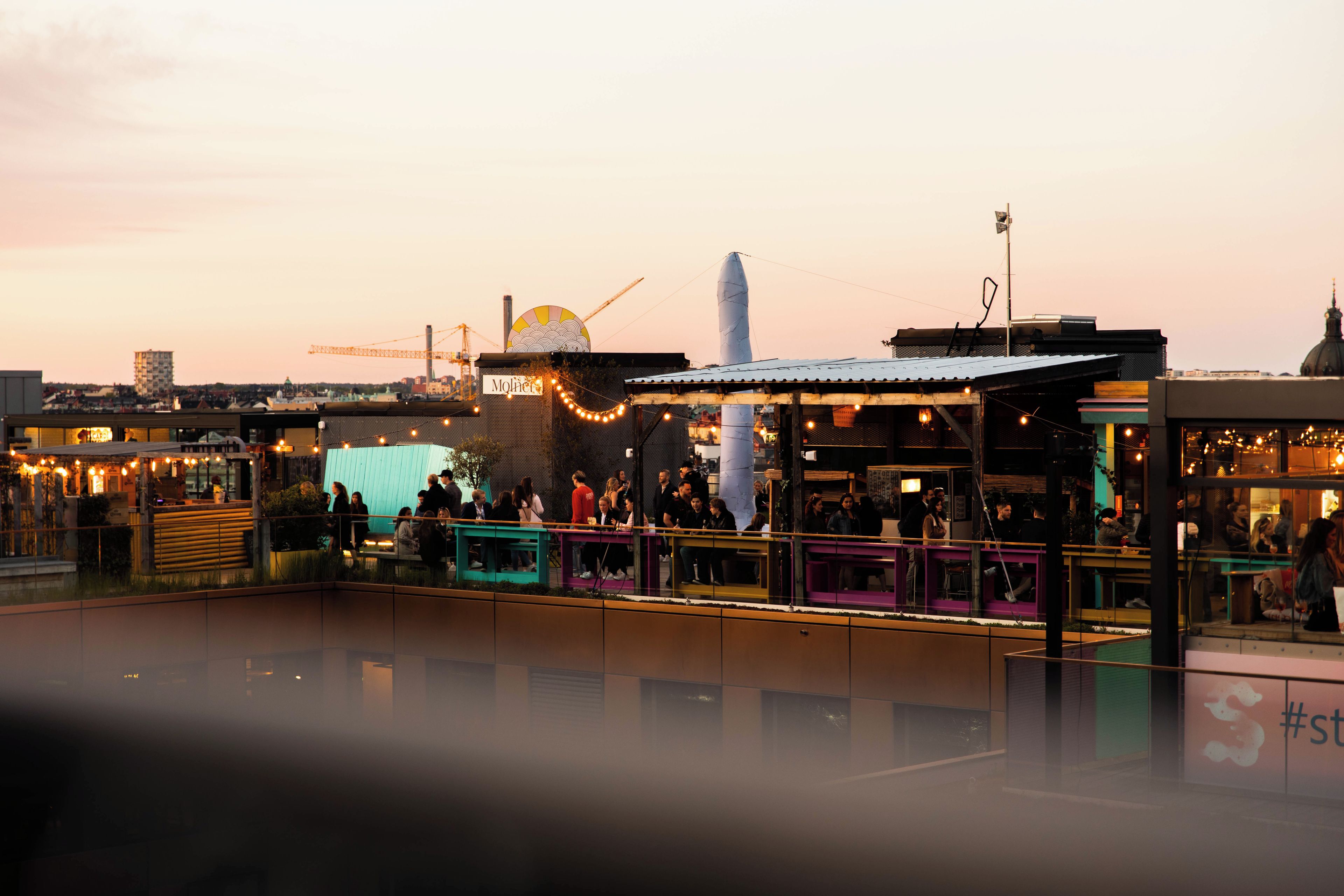 Un bar en la azotea con mesas al aire libre, una gran escultura blanca y vistas del horizonte de la ciudad.