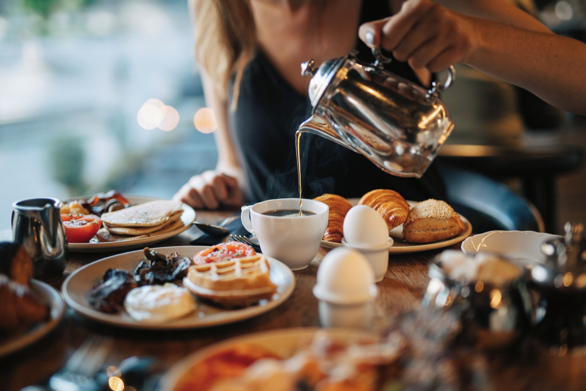 Une table mise pour le petit-déjeuner, avec différents plats, et une personne en train de verser une boisson.