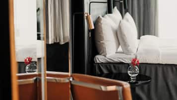 Una camera d'albergo con un letto, un comodino con un vaso di fiori, una sedia e uno specchio che riflette l'ambiente.