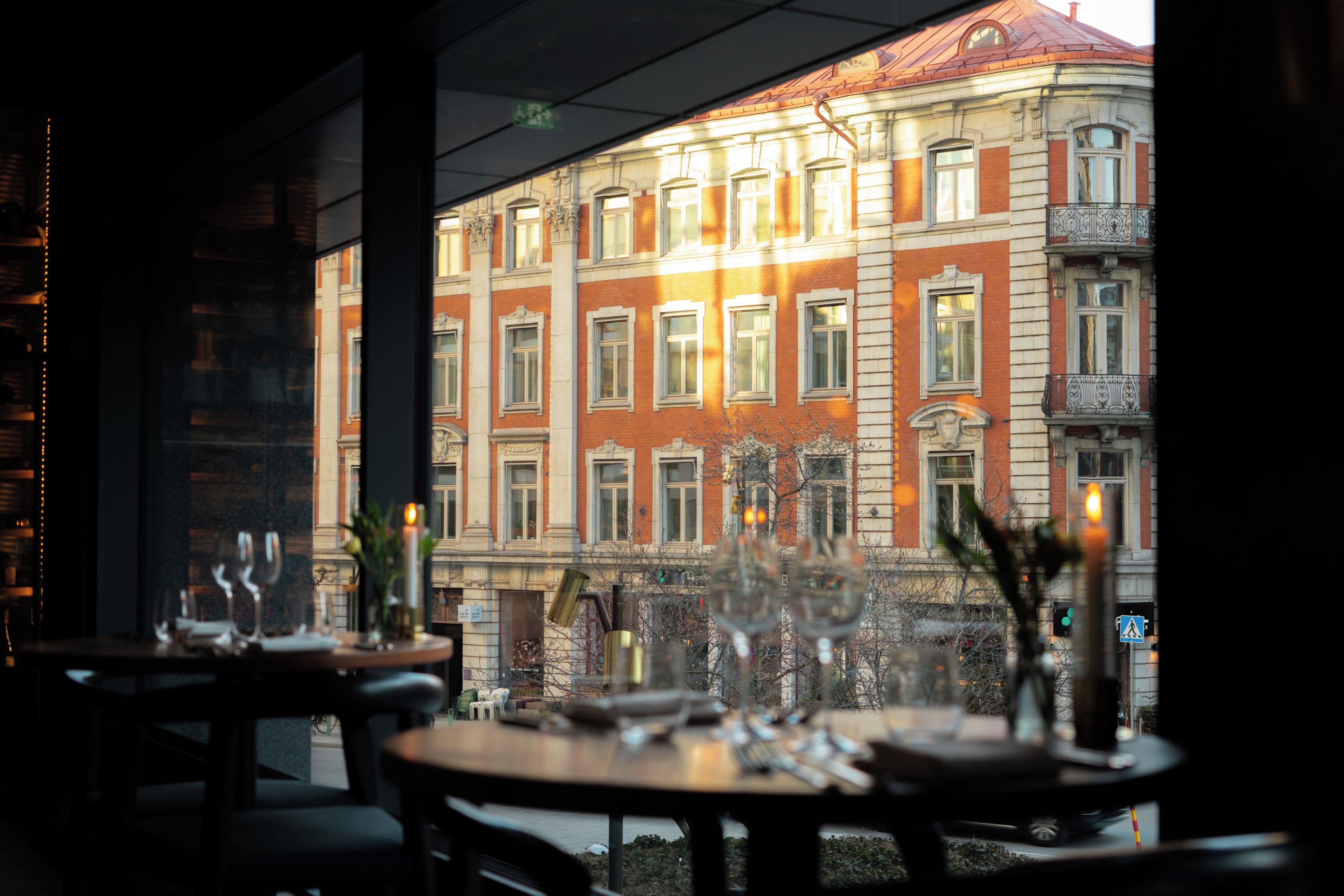 Un restaurante con mesas dispuestas para comer, vista de un edificio histórico con varias ventanas, y una señal de paso para peatones al frente.