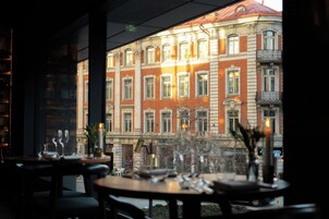 Ein Restaurant mit gedeckten Tischen, Blick auf ein historisches Gebäude mit zahlreichen Fenstern und ein Fußgängerübergang im Vordergrund.