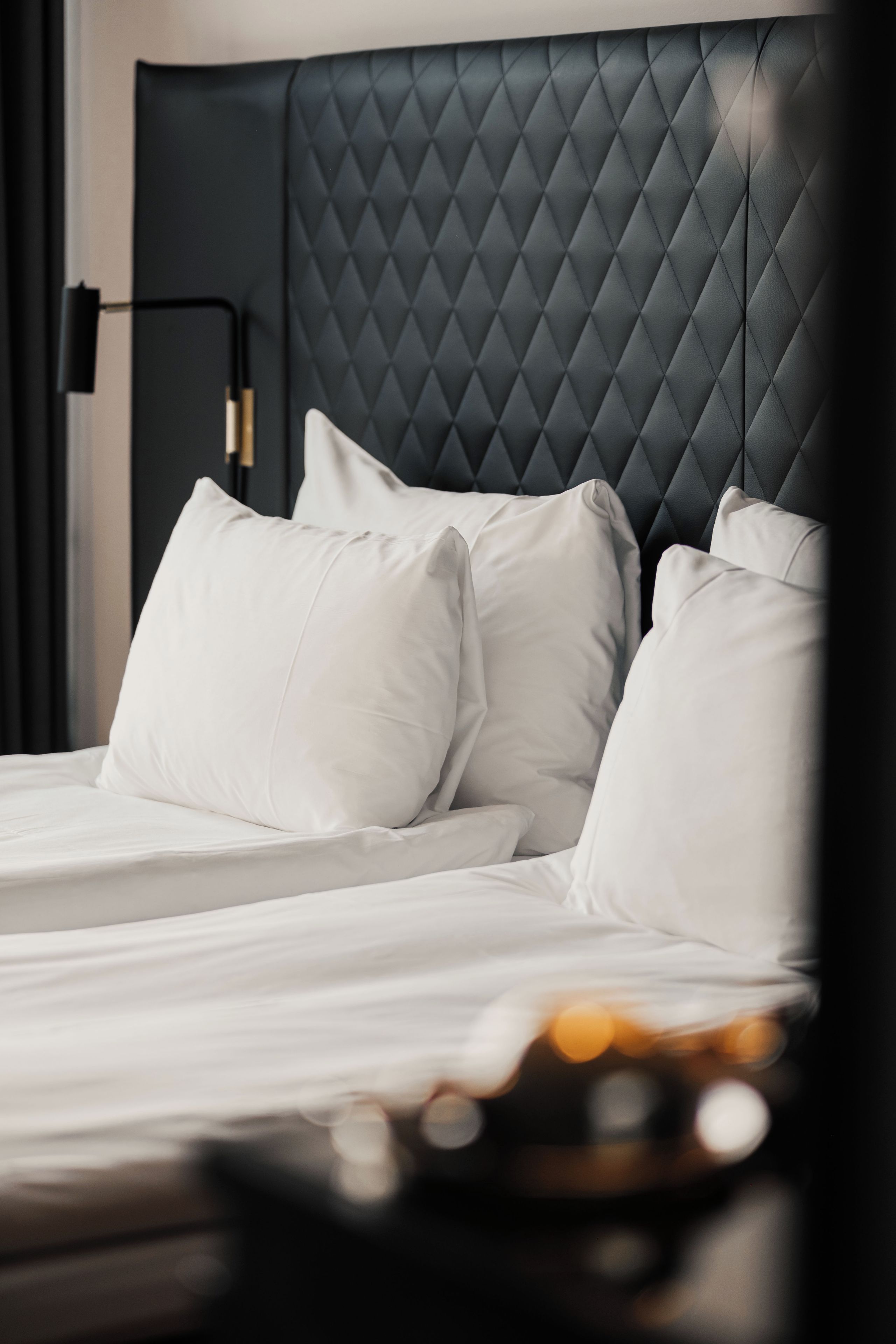A bed with white linens and pillows, a dark headboard, and a nightstand with a lamp.