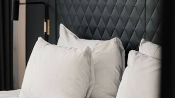 A bed with white linens and pillows, a dark headboard, and a nightstand with a lamp.
