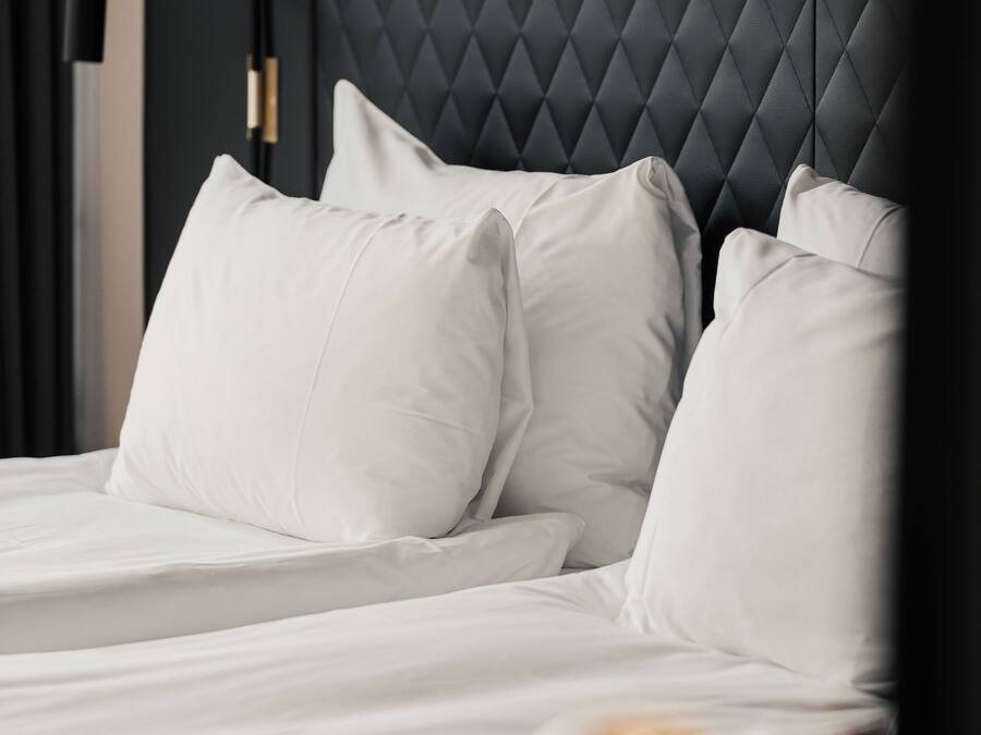 A bed with white linens and pillows, a dark headboard, and a nightstand with a lamp.