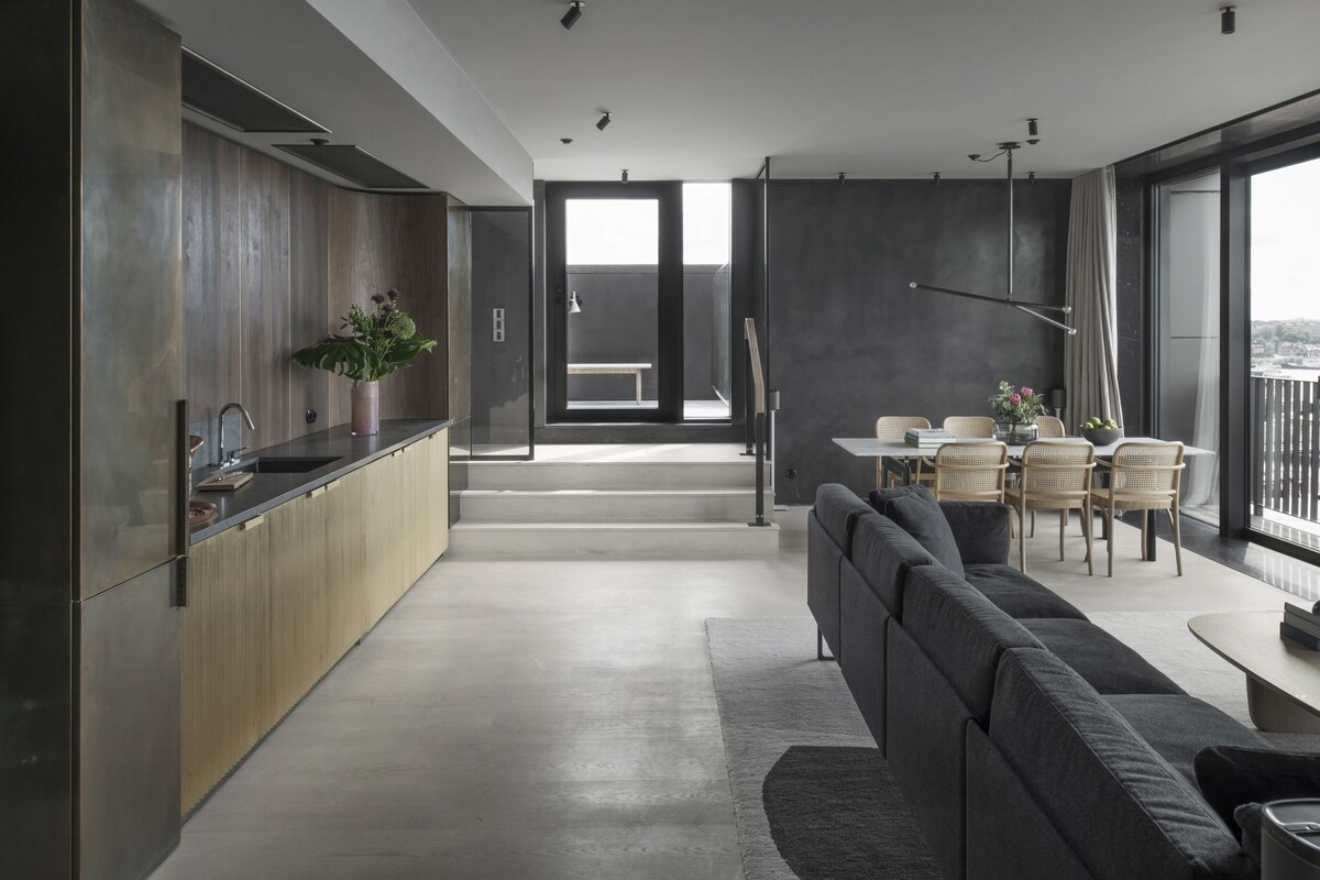 A modern kitchen with a wooden countertop and a sink, a dining area with a table and chairs, and a large window providing a view of the city.