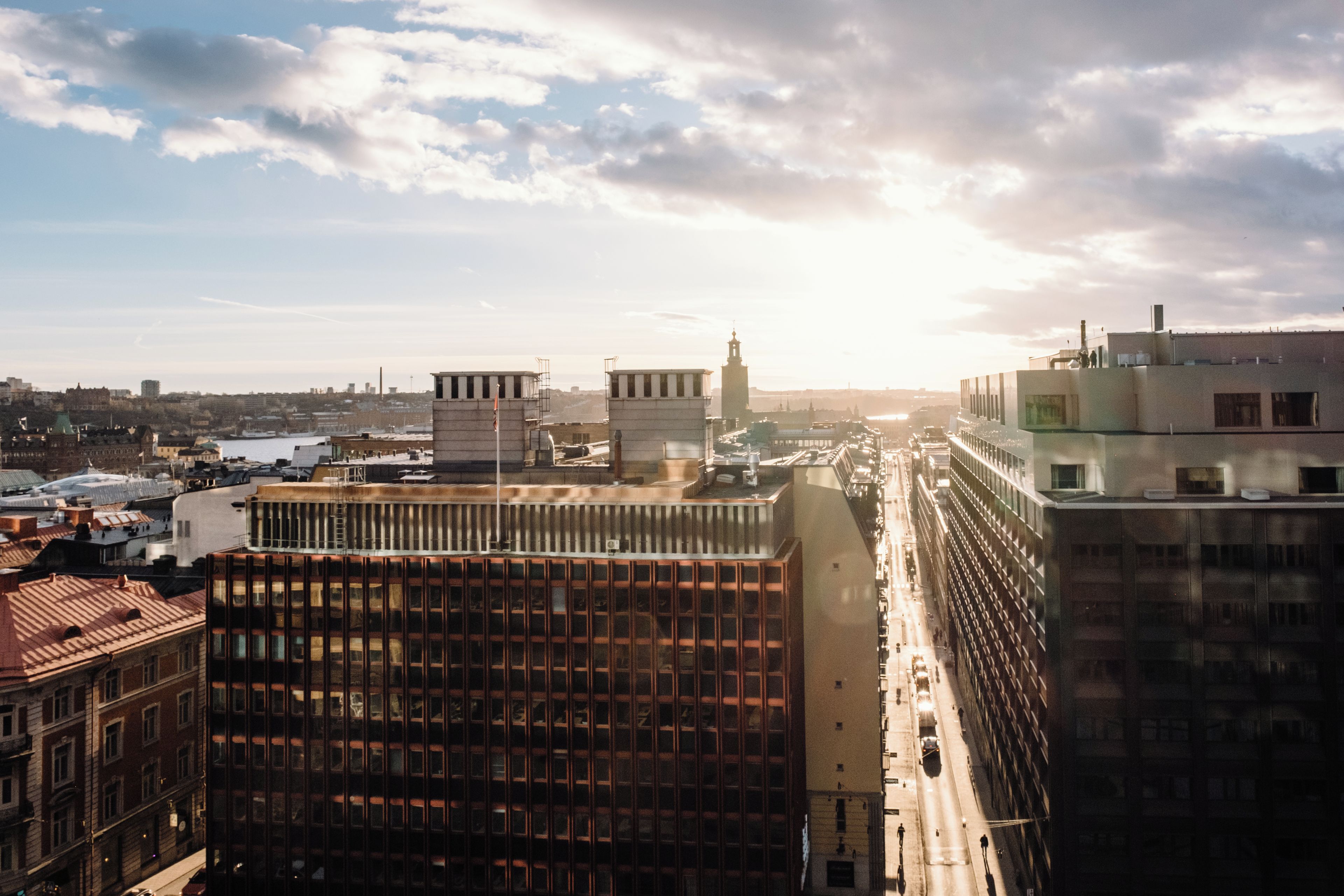 A cityscape with modern buildings, a clear sky, and a distant view of a body of water.
