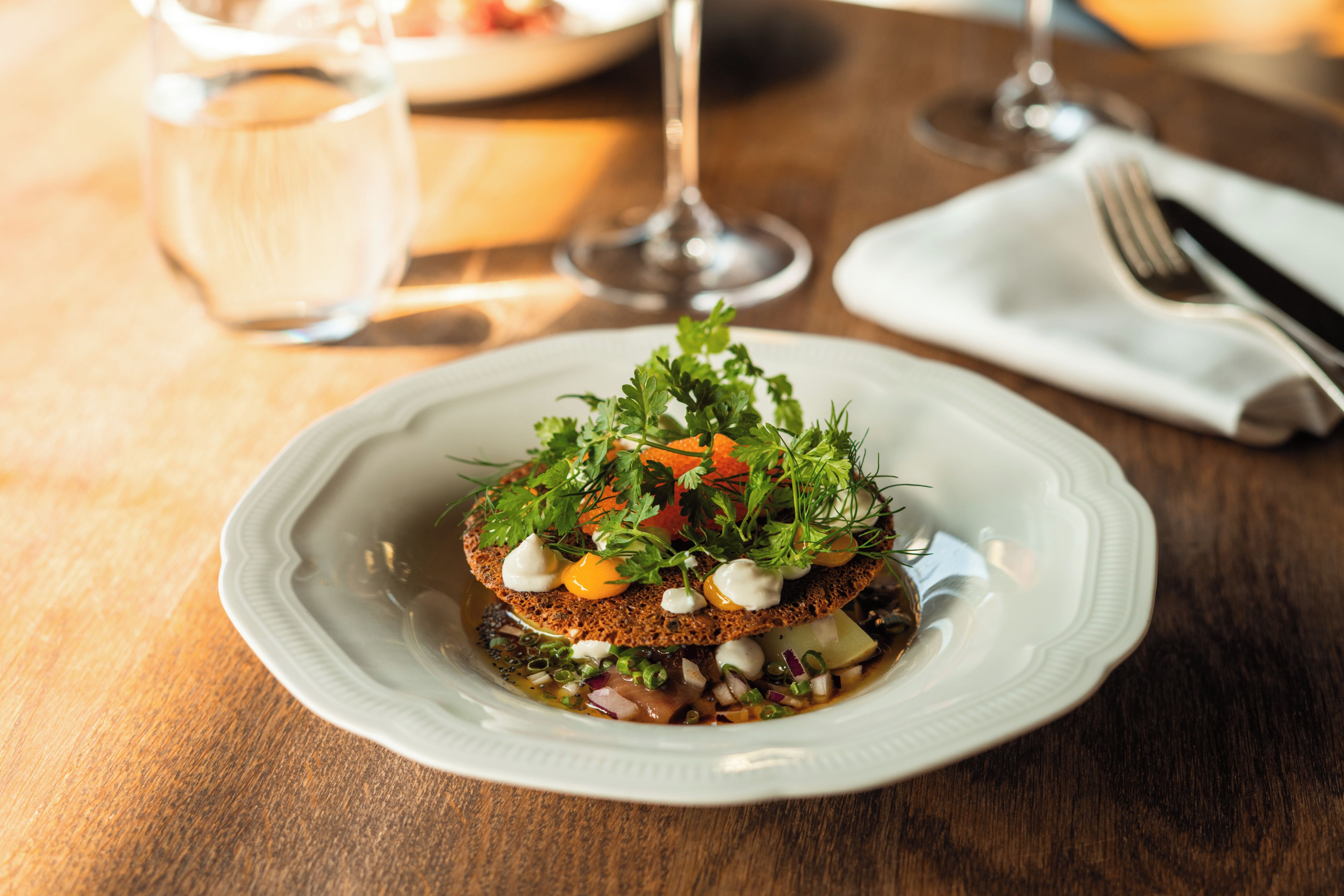 A plate of food with a variety of toppings and a glass of water on a wooden table.