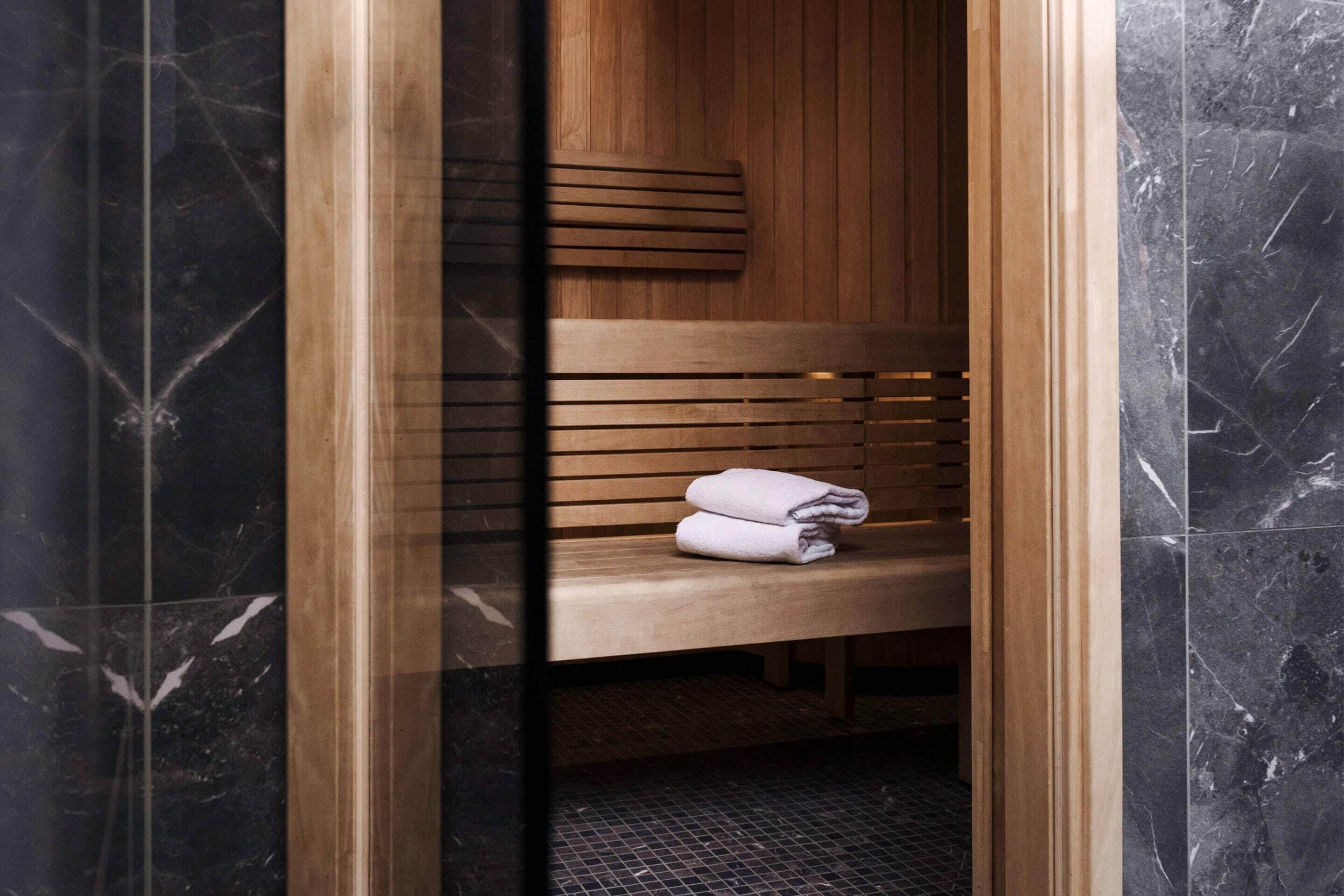 A sauna with a wooden bench and a towel, enclosed by dark marble walls.