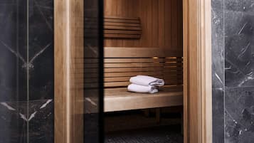 A sauna with a wooden bench and a towel, enclosed by dark marble walls.