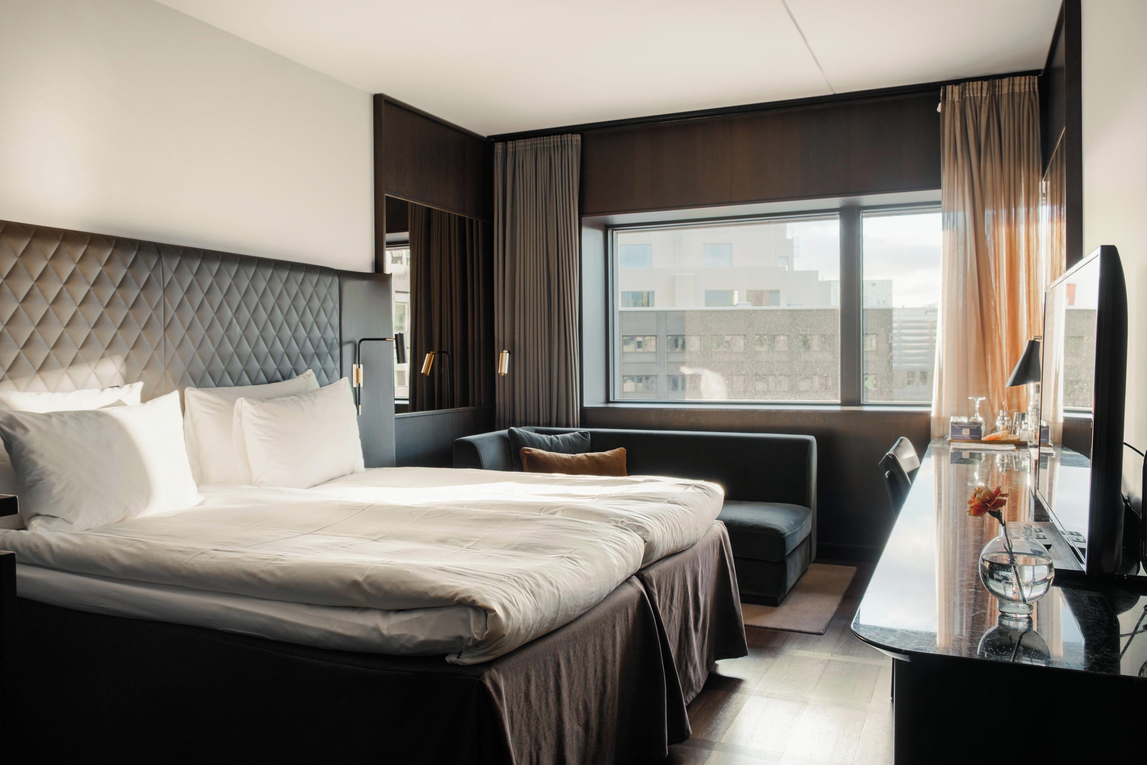 Habitación de hotel con una cama grande, zona de estar, escritorio y ventana con vistas a edificios.