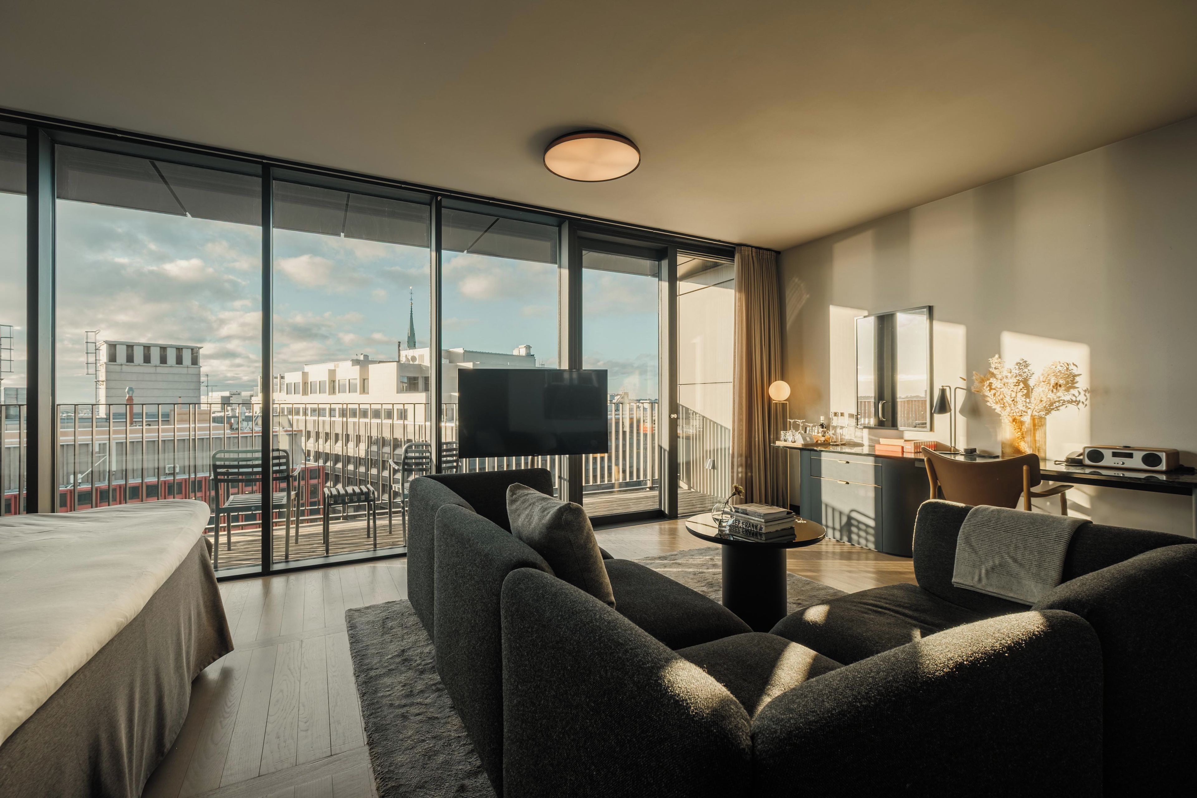 A modern living room with a large window, a flat-screen TV, a sofa, a coffee table, and a kitchen area with a radio.