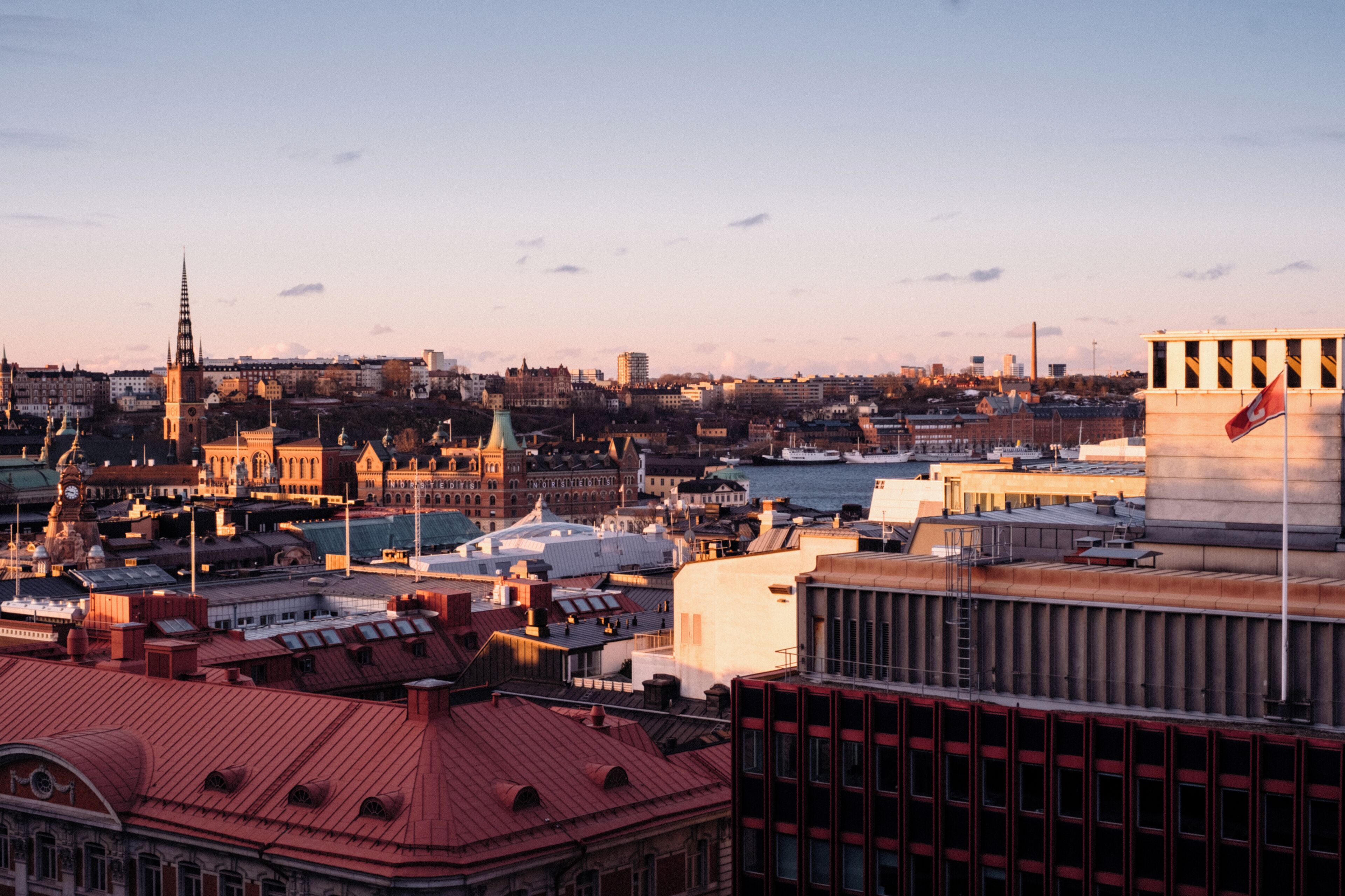 A cityscape with historic buildings, a prominent church spire, and a modern building with a flag.
