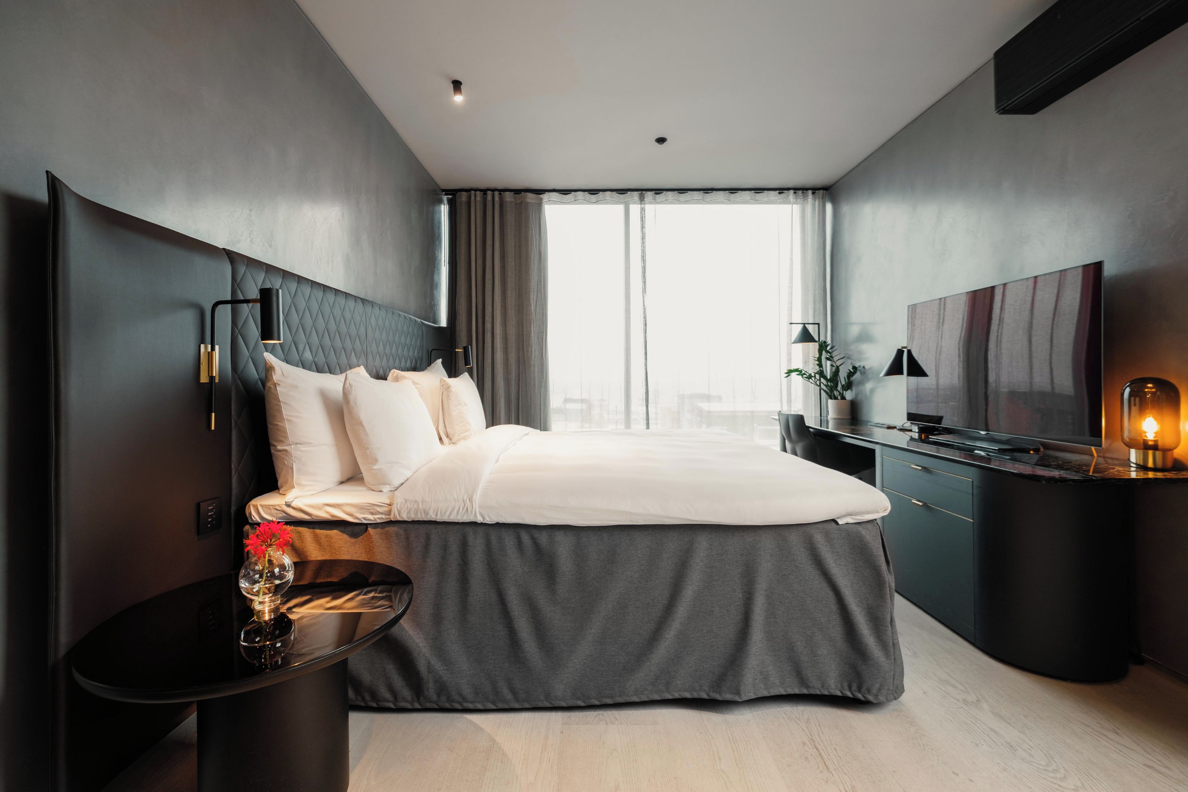 A modern hotel room with a large bed, a desk, a TV, and a view of the city.
