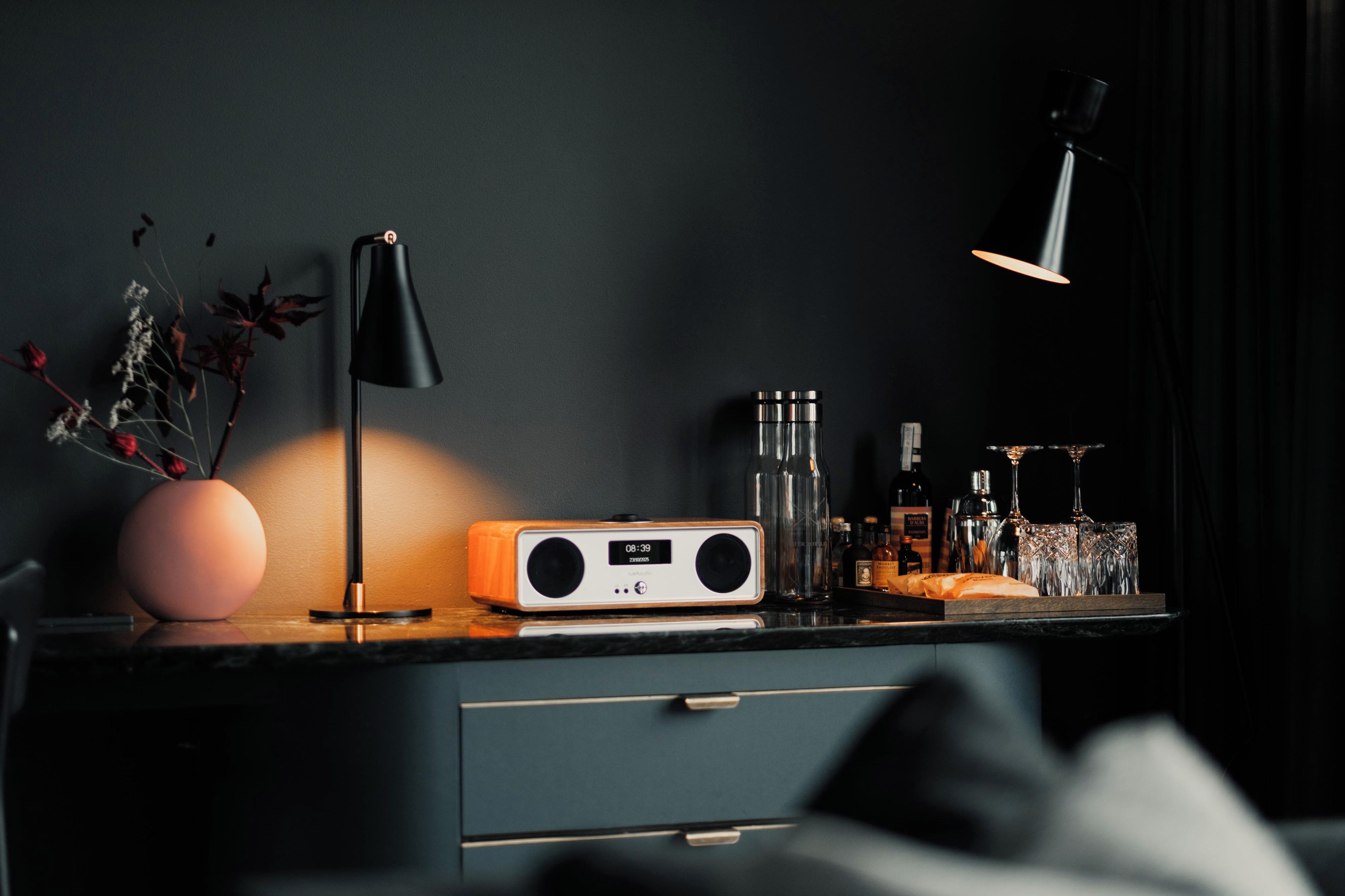 A modern interior with a dark wall, a desk with a radio, a lamp, and various bottles.