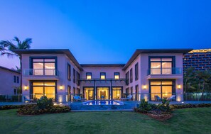 A modern two-story house with a swimming pool, large windows, and a well-lit entrance.