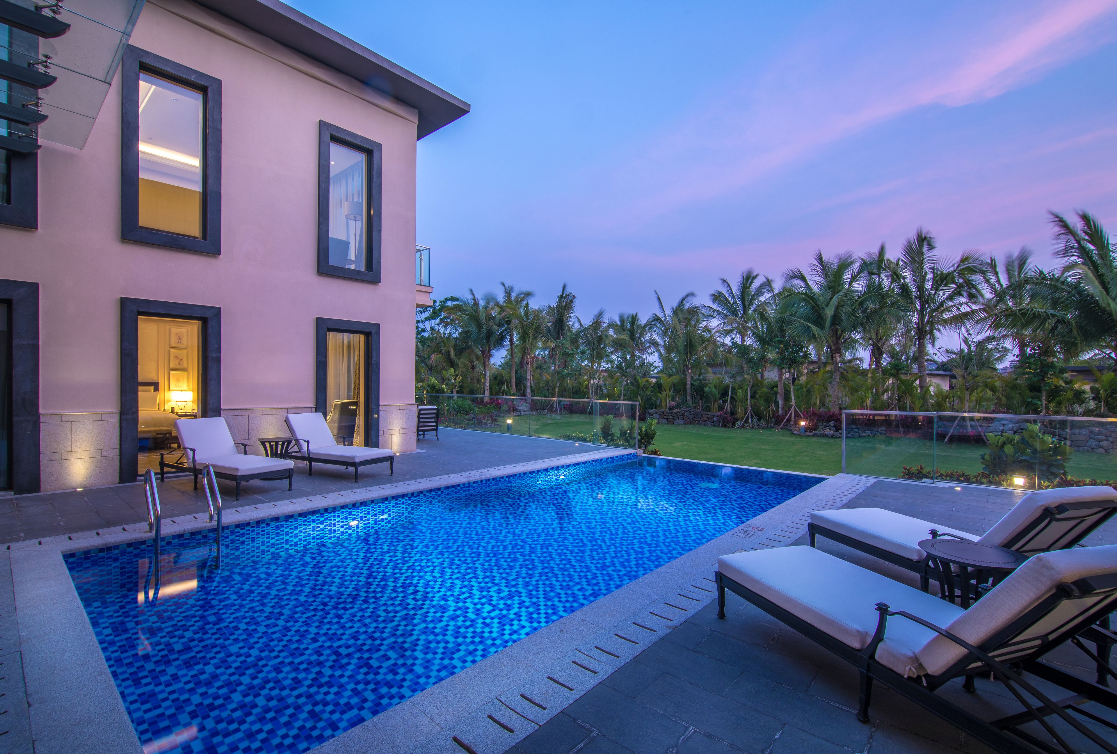 A modern pool area with lounge chairs, a clear blue pool, and a view of palm trees.