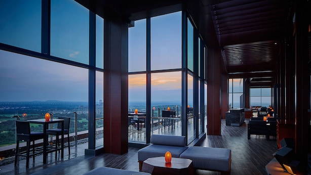 A modern lounge with large windows offering a city view, comfortable seating, and a bar area. - The Ritz-Carlton, Haikou (Haikou)