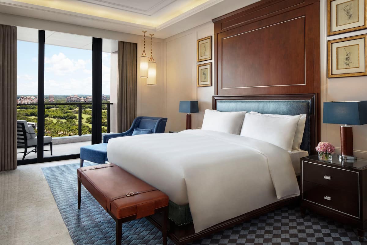 A hotel room with a large bed, a desk, a chair, a nightstand, and a view of the city.