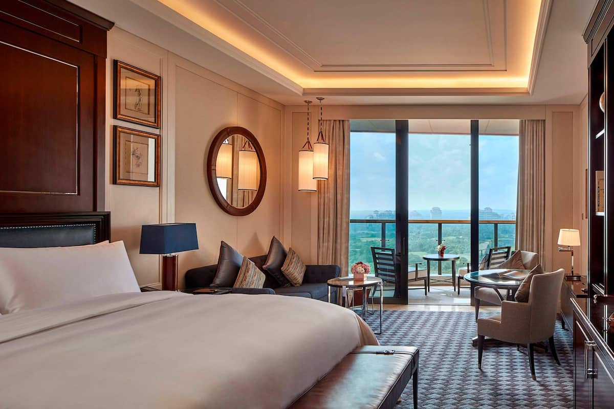 A hotel room with a large bed, a sofa, a dining table, and a balcony with a view.