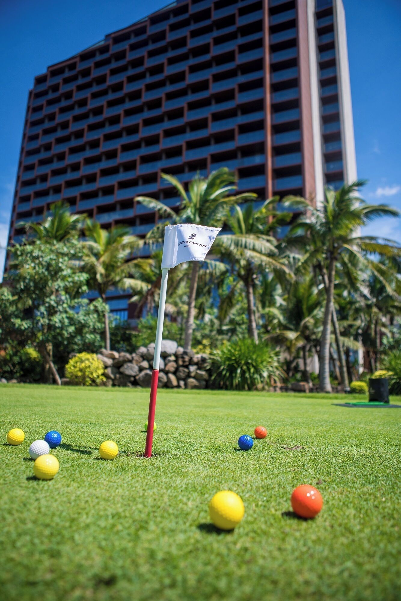A golf course with a flagstick in the foreground and a tall building in the background.