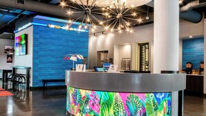 A modern reception desk with a colorful LED display, a ceiling with a geometric light fixture, and a wall-mounted television.