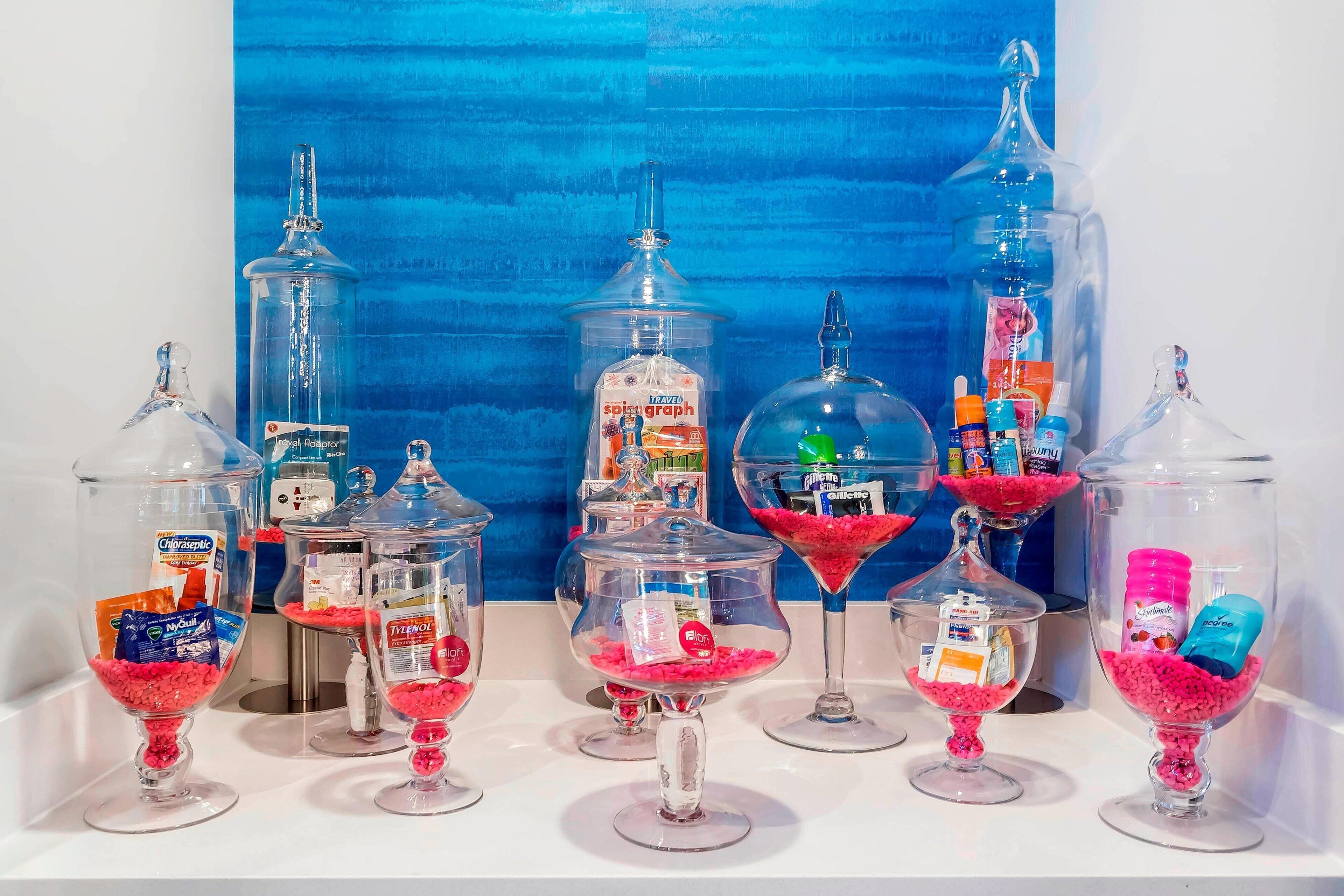 Una presentación de varios recipientes de vidrio con diferentes objetos en su interior, incluyendo bocadillos y botellas pequeñas, sobre un fondo azul.