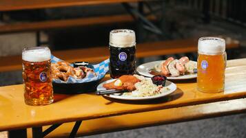 Una mesa de madera con tres vasos de cerveza, un cesto de pretzels y platos de comida que incluyen salchichas y chucrut.