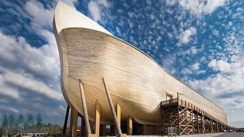 A large wooden boat-like structure with a curved hull, supported by wooden pillars, set against a clear sky.