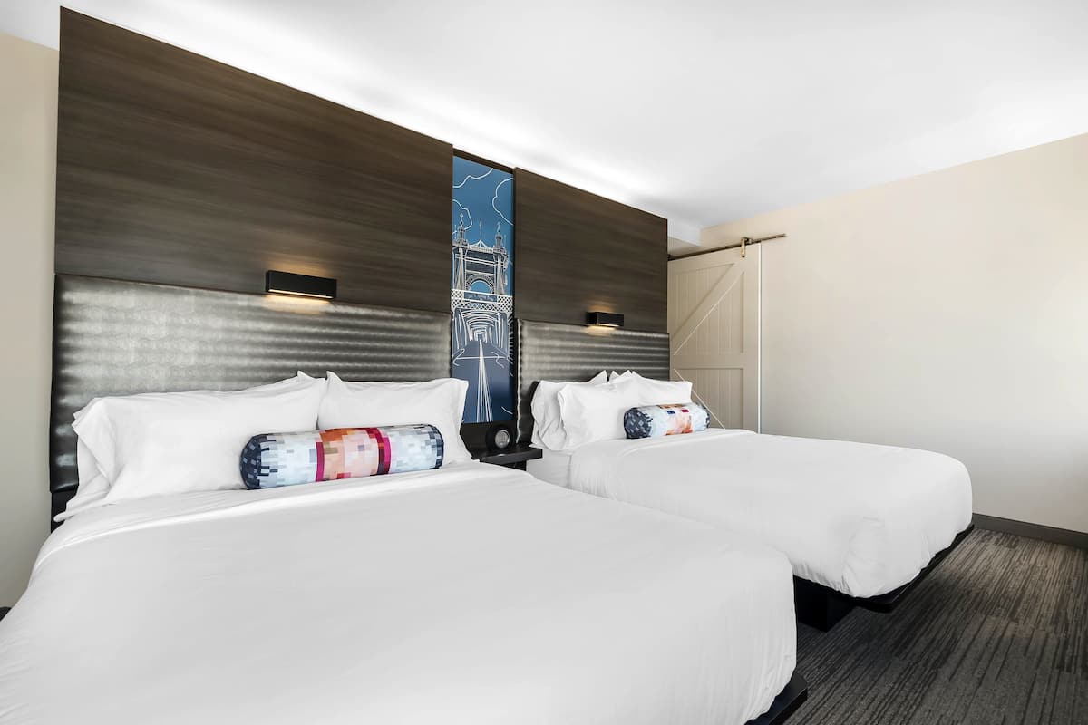 Habitación de hotel con dos camas, una obra de arte grande en la pared y un diseño moderno para la cabecera.