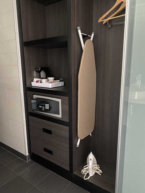 Una habitación de hotel moderna con armario empotrado, cafetera, secador de pelo y un pequeño estante con artículos de aseo.