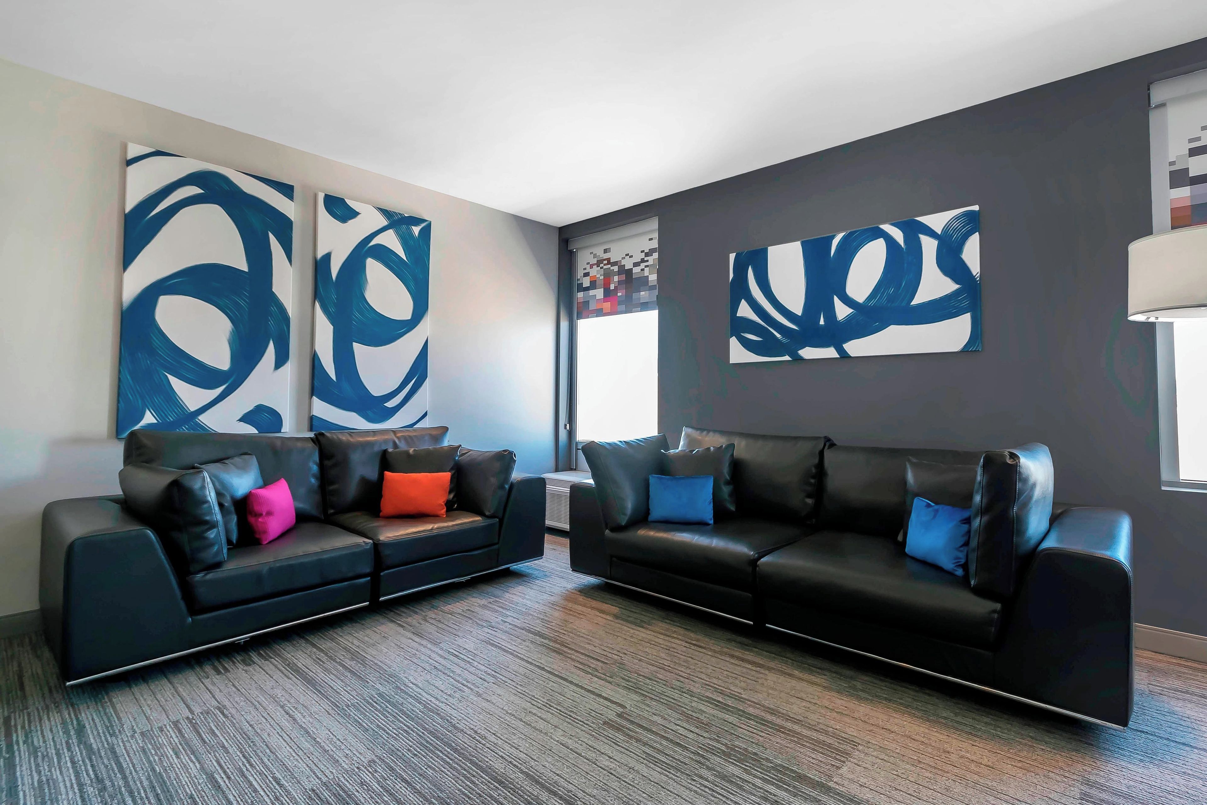 A modern living room with two black leather sofas, colorful cushions, and abstract wall art.