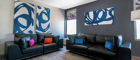 A modern living room with two black leather sofas, colorful cushions, and abstract wall art.