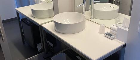A modern bathroom with two round sinks, a mirror, and a trash bin.